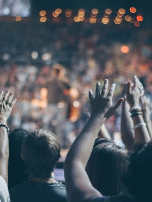 Energetic crowd at a live concert with hands raised and bright lights.